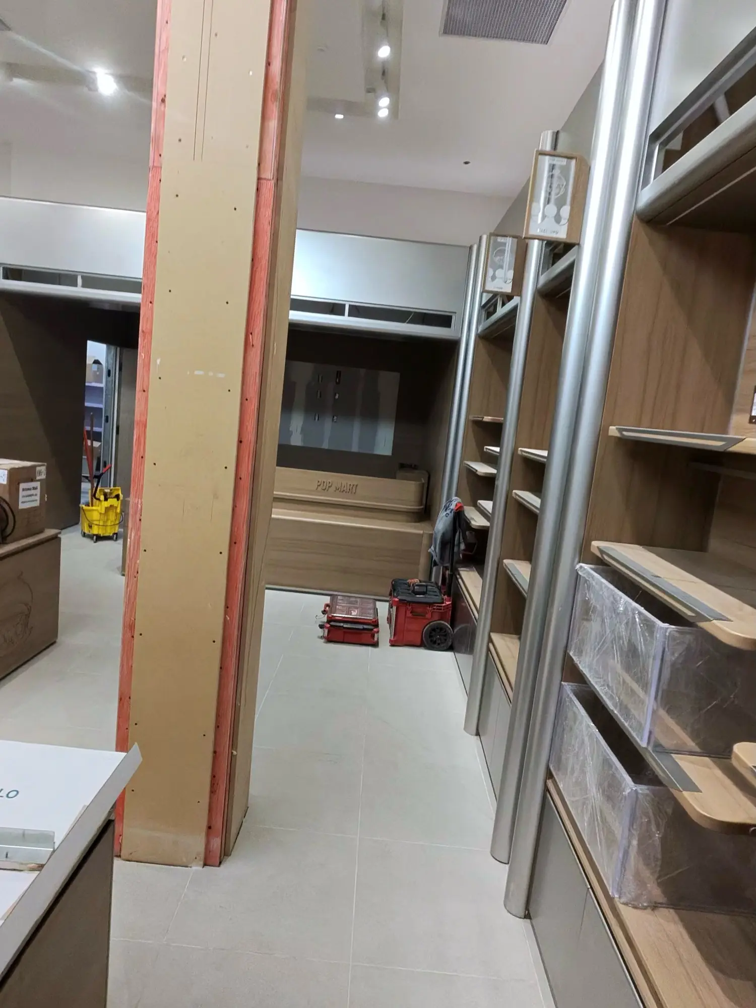 A retail fit-out at substantial completion: a wrapped column, open fixtures, cords and tools on the floor.