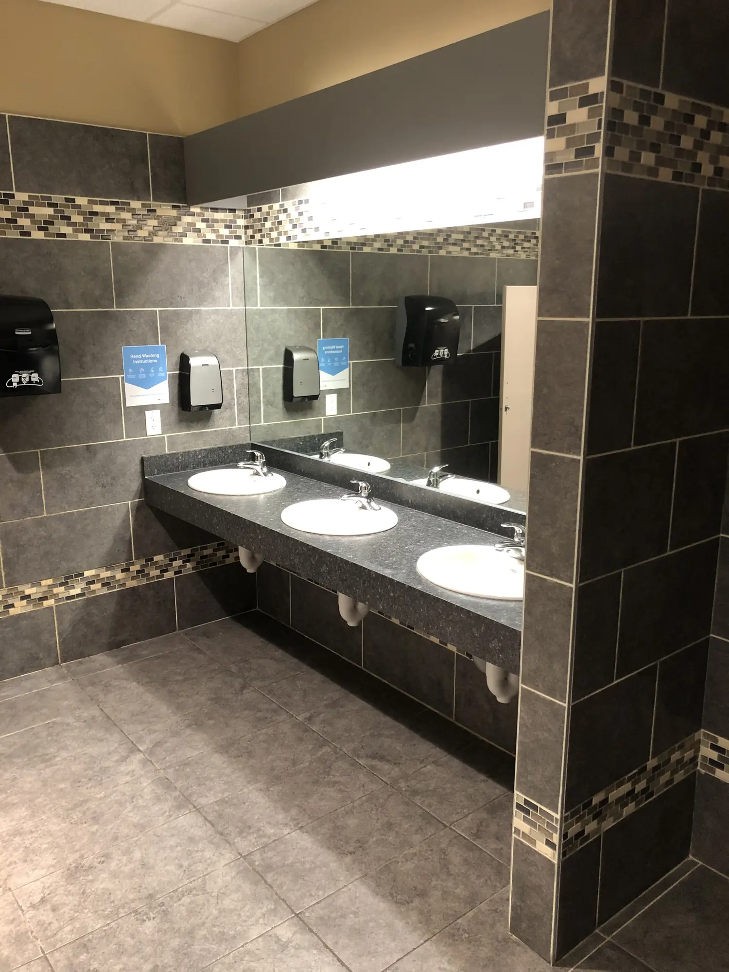 A tiled restroom with a three-sink vanity, clean.